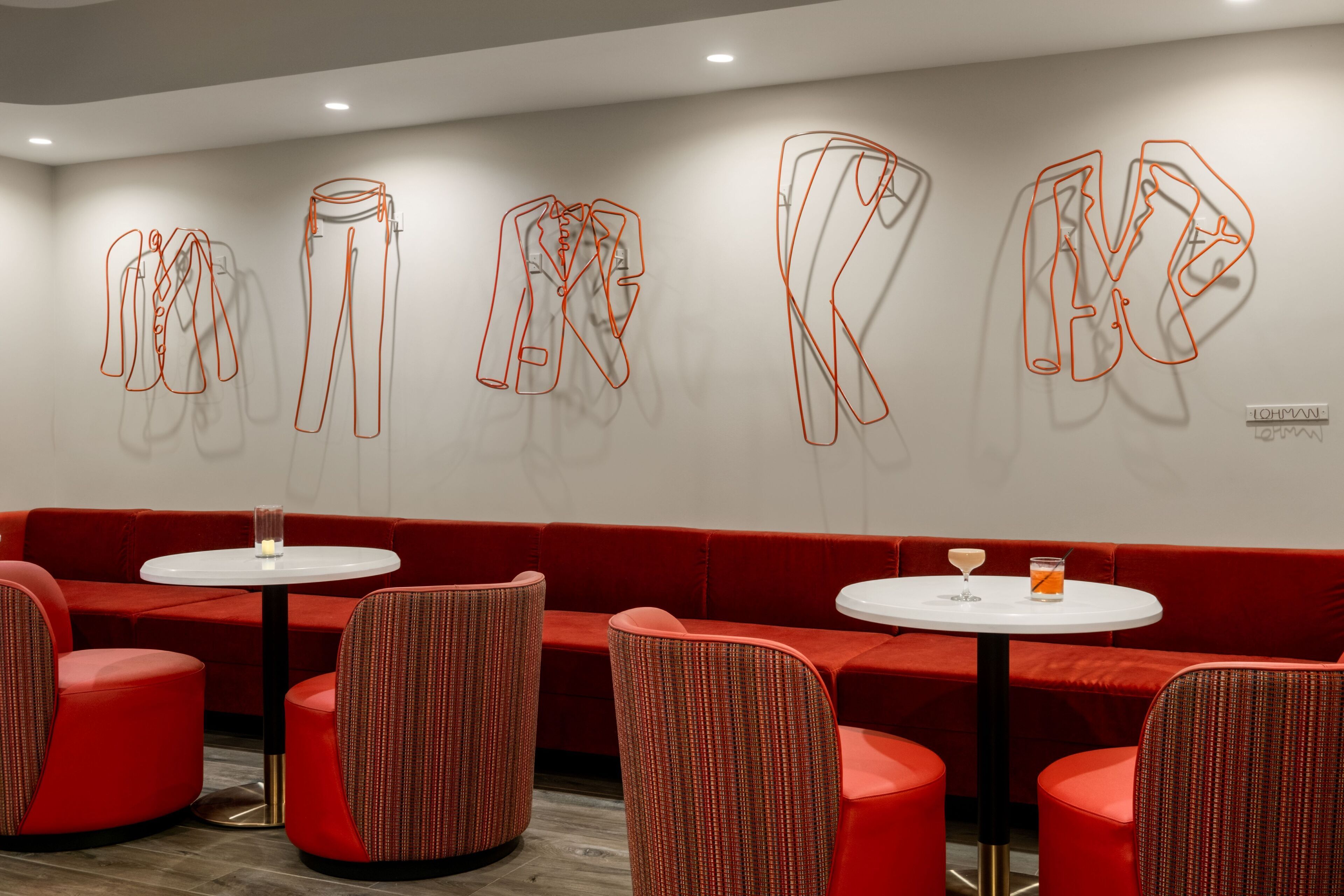 A modern interior with red upholstered seating, white tables, and abstract art on the walls.