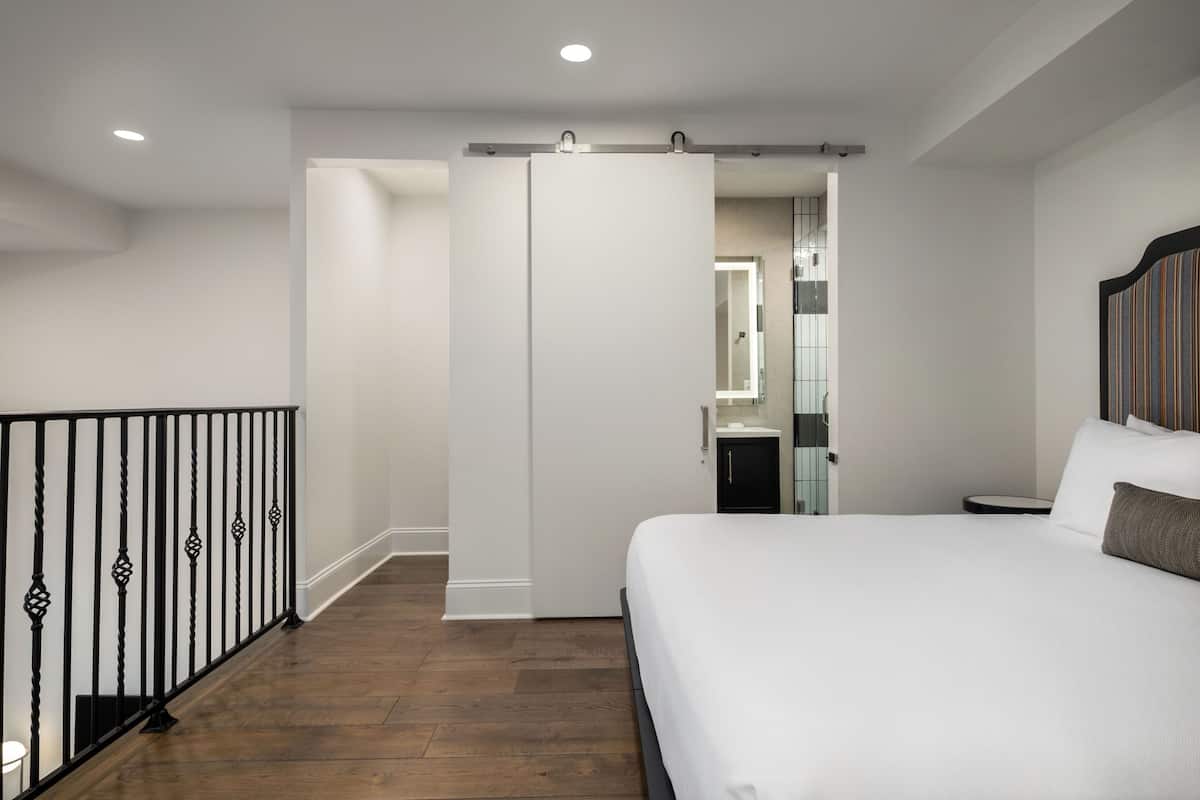 Ein modernes Hotelzimmer mit einem großen Bett, einem Kleiderschrank, einem kleinen Badezimmer und einem Balkon mit Geländer.