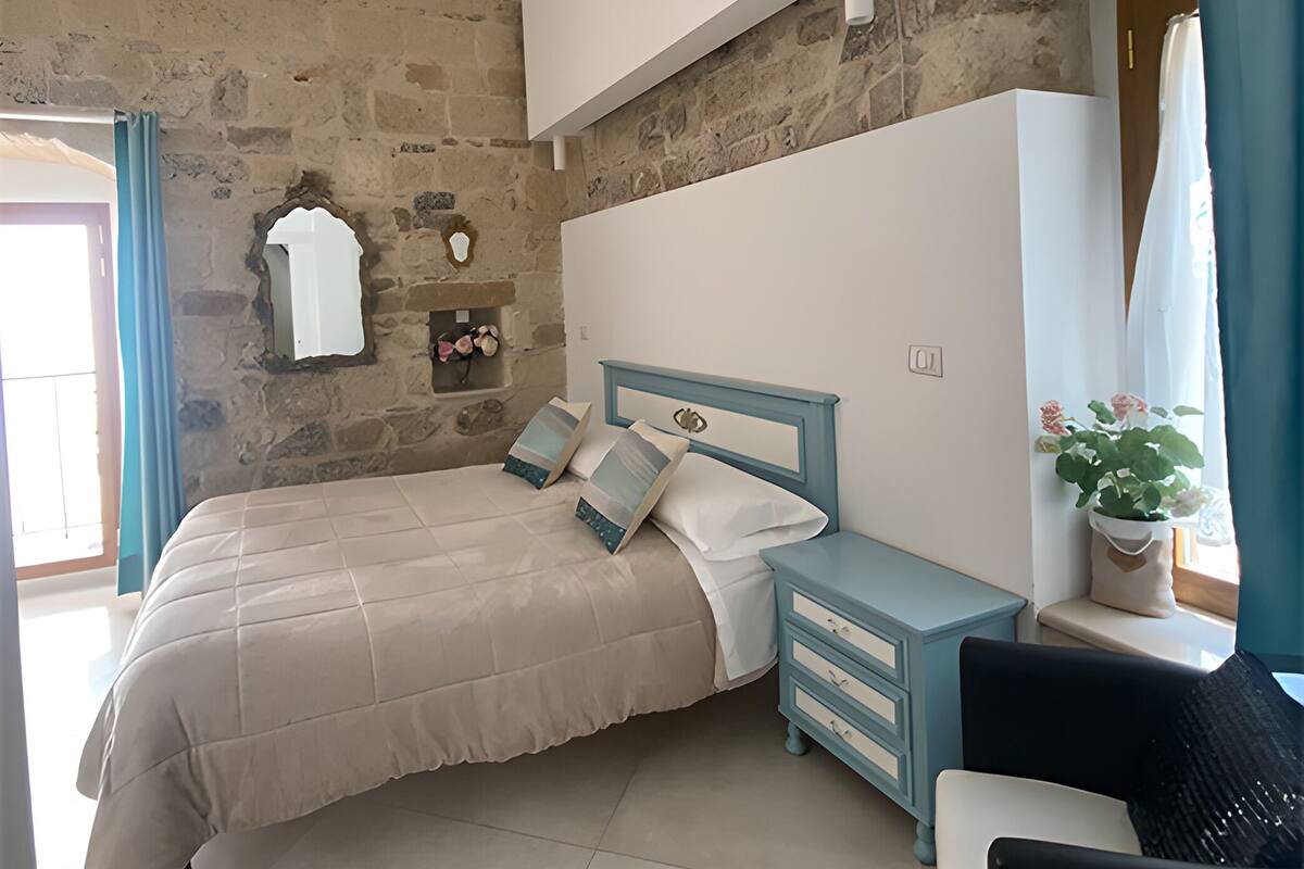 Une chambre à coucher avec un lit, une table de chevet, une chaise et un mur en pierre.