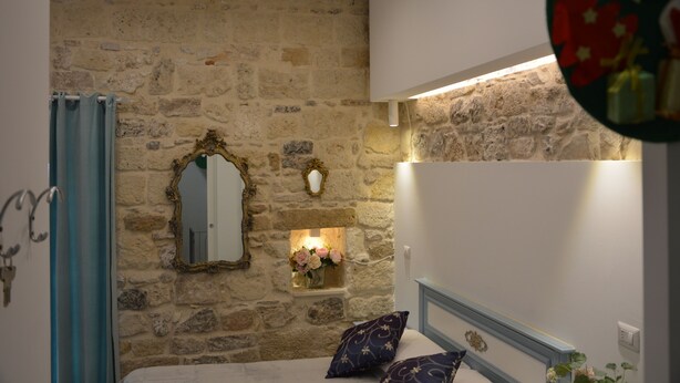 A bedroom with a stone wall, a mirror, a bedside table with flowers, and a bed with patterned pillows. - AFFITTACAMERE DIMORA DEL CARMINE (Bari)