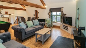 A cozy living room with a grey sofa, a wooden coffee table, a television, and a fireplace. - The Barn by Lyons (Talybont)