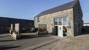 A stone building with a sloped roof, a glass door entrance, and a sign reading "Welcome to the Barn." - The Barn by Lyons (Talybont)