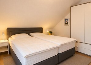 A bedroom with a bed, bedside tables, a nightstand, a lamp, a potted plant, and a wardrobe.