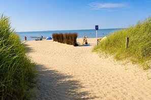 A sandy beach path leading to the sea with tents and people.