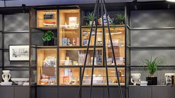 Un interior moderno con una mesa de vidrio central rodeada de asientos acolchados azules, una estructura metálica escalonada y una estantería con diversos objetos.