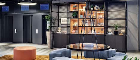A modern lobby with a central seating area, a reception desk, and a display of items on shelves.