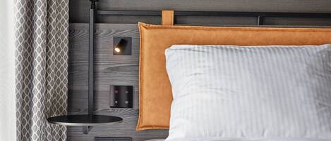 Un dormitorio moderno con cabecera de madera, una mesita de noche con lámpara y un enchufe.