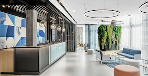 A modern interior with a reception desk, seating area, and a green wall with plants. - Hotel Wien-Schönbrunn (Vienna)