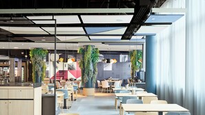 Une cafétéria moderne avec de longues tables et des chaises, un espace de service central et des plantes décoratives.