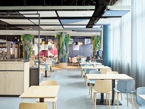 A modern cafeteria with long tables and chairs, a central serving area, and decorative plants. - Hotel Wien-Schönbrunn (Vienna)