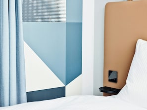 A modern hotel room with a bed, a bedside table with a phone, and a geometric-patterned wall. - Hotel Wien-Schönbrunn (Vienna)