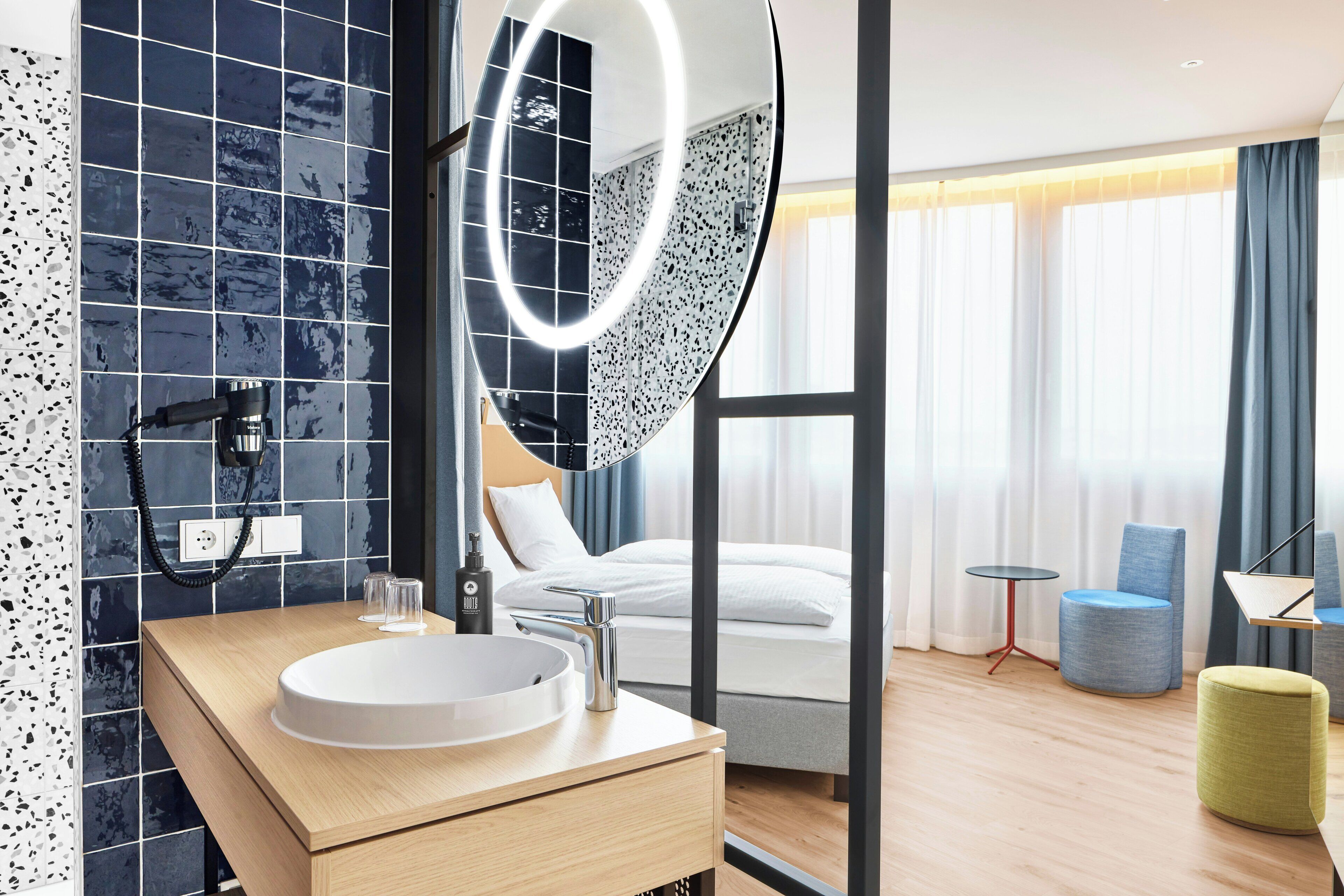 Een moderne hotelbadkamer met een grote spiegel, een rond wastafel en een handdouche.