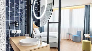 Een moderne hotelbadkamer met een grote spiegel, een rond wastafel en een handdouche.