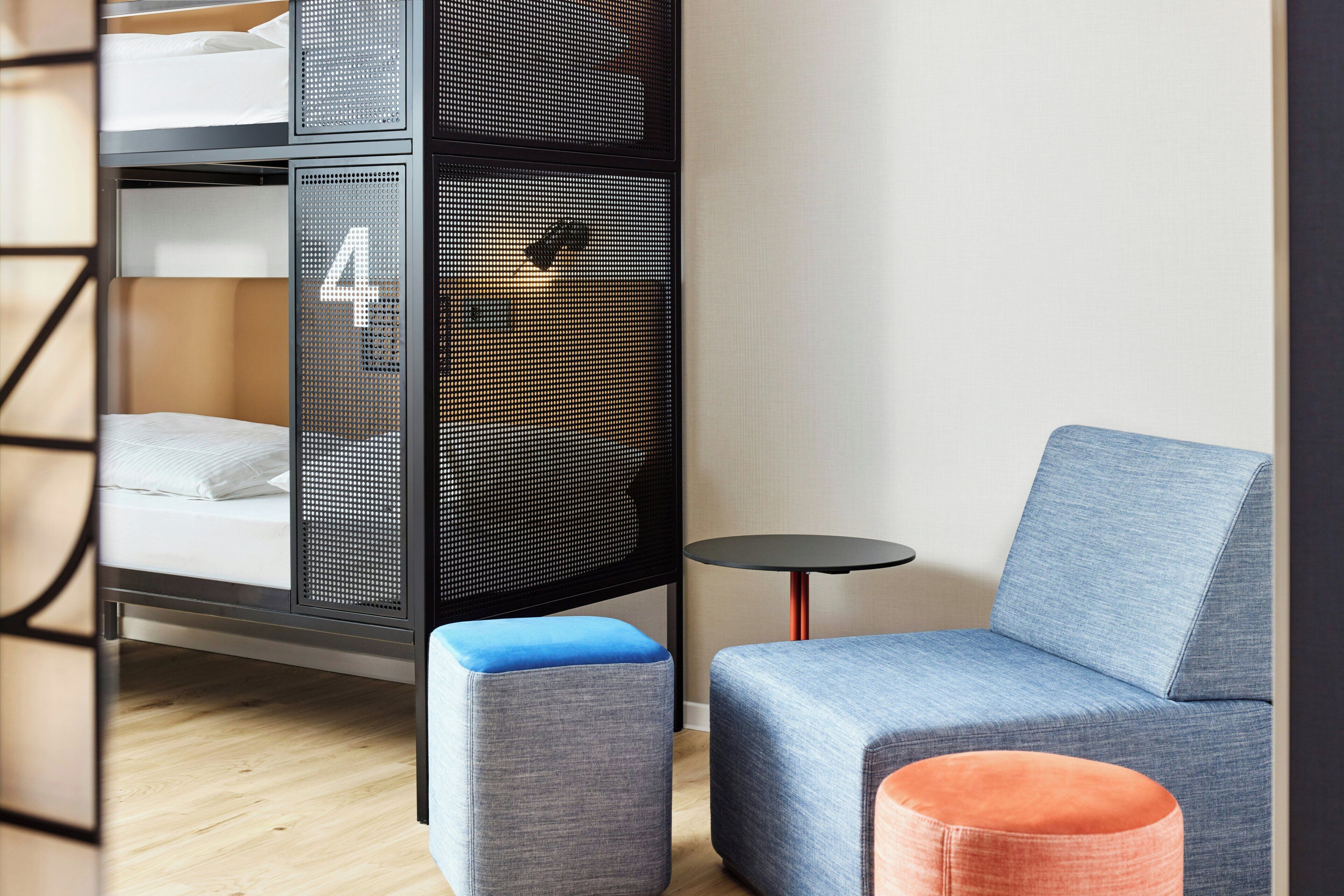 Ein modernes Zimmer mit einem Etagenbett, einem kleinen runden Tisch und einem grauen Sofa mit blauer Kissen.