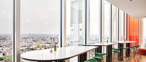 A modern bar area with high-rise city views, large windows, and green bar stools.