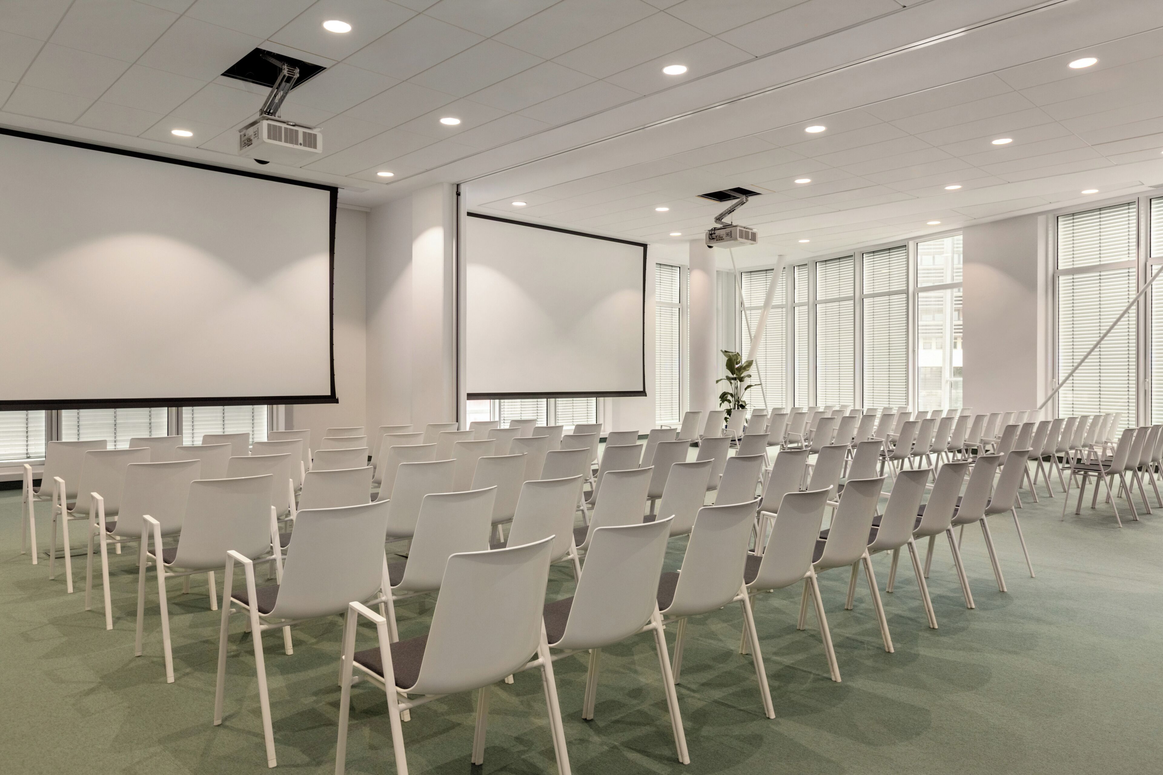 A conference room with rows of white chairs, a large screen, and a projector mounted on the ceiling.