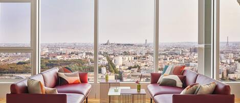 A modern living room with a city view, featuring two leather sofas, a coffee table, and a vase with flowers.