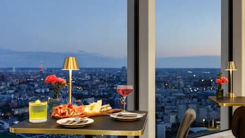 Una mesa servida con comida y bebidas, vista a la ciudad y una lámpara.