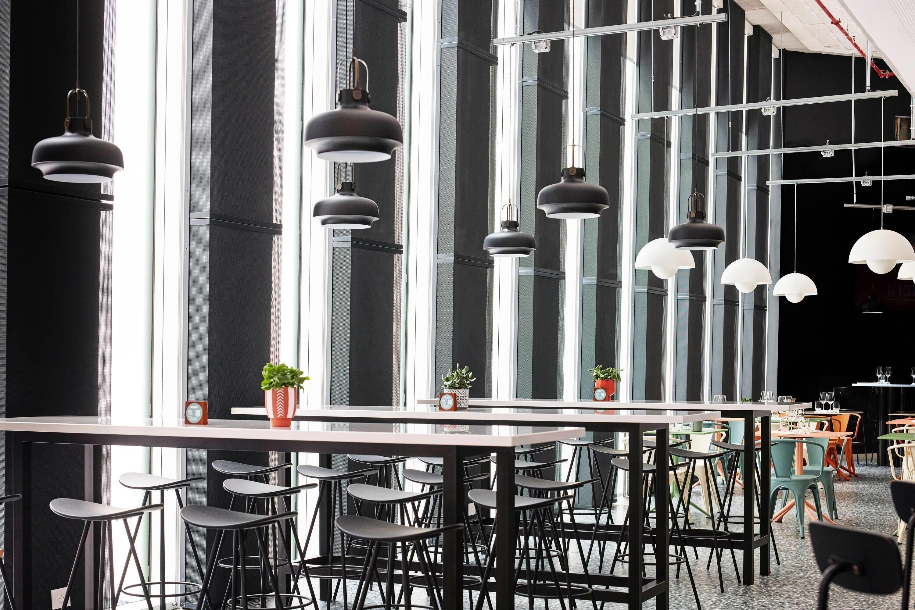 A modern bar area with multiple seating arrangements and pendant lighting.