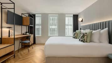 Une chambre d’hôtel avec un lit, un bureau et une chaise, une télévision et des fenêtres.