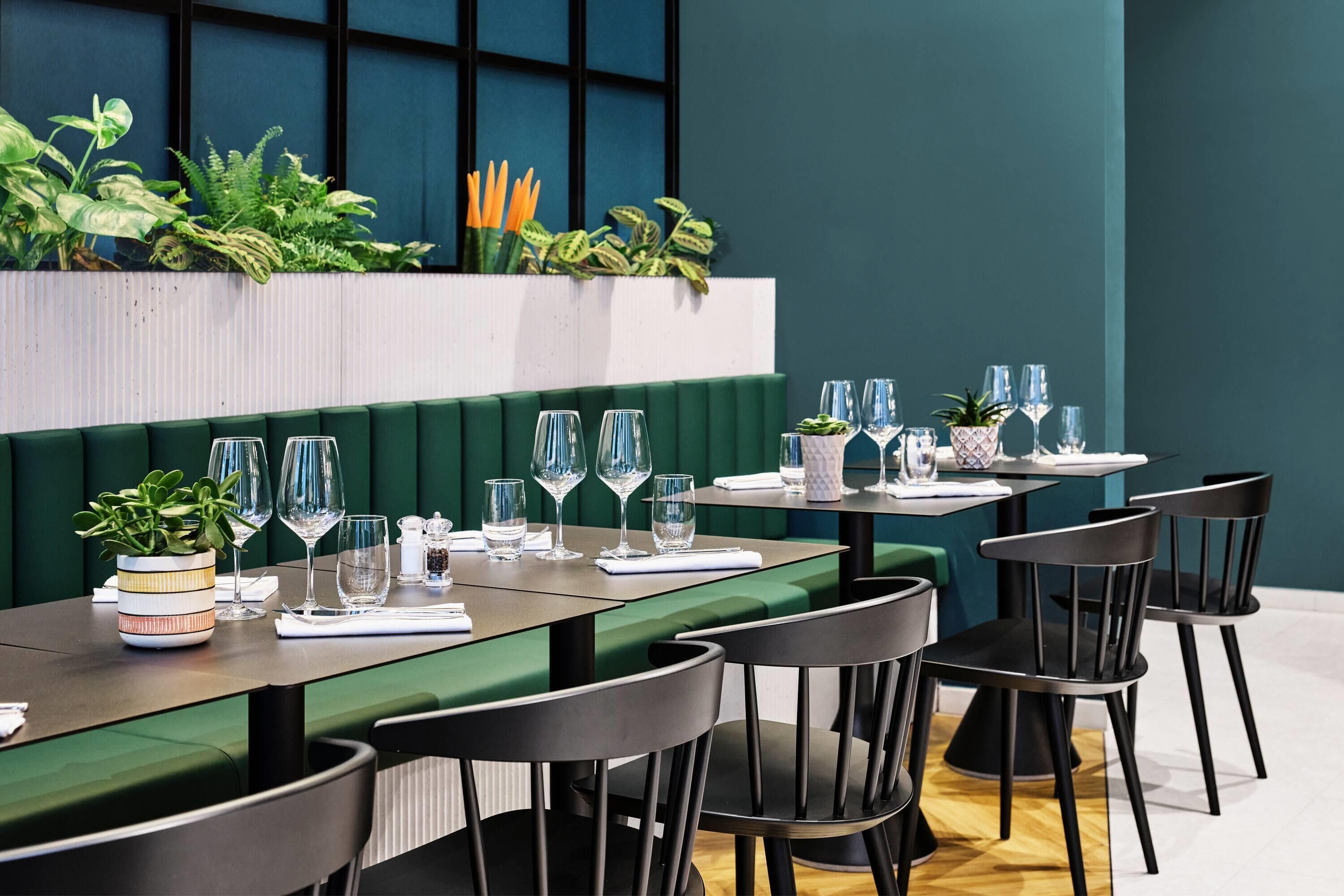 Un restaurant avec des banquettes vertes, des chaises noires et une variété de plantes.