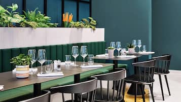 Un restaurante con asientos tipo banca verdes, sillas negras y una variedad de plantas.