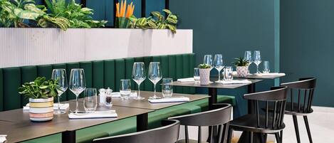 Un restaurante con asientos tipo banca verdes, sillas negras y una variedad de plantas.