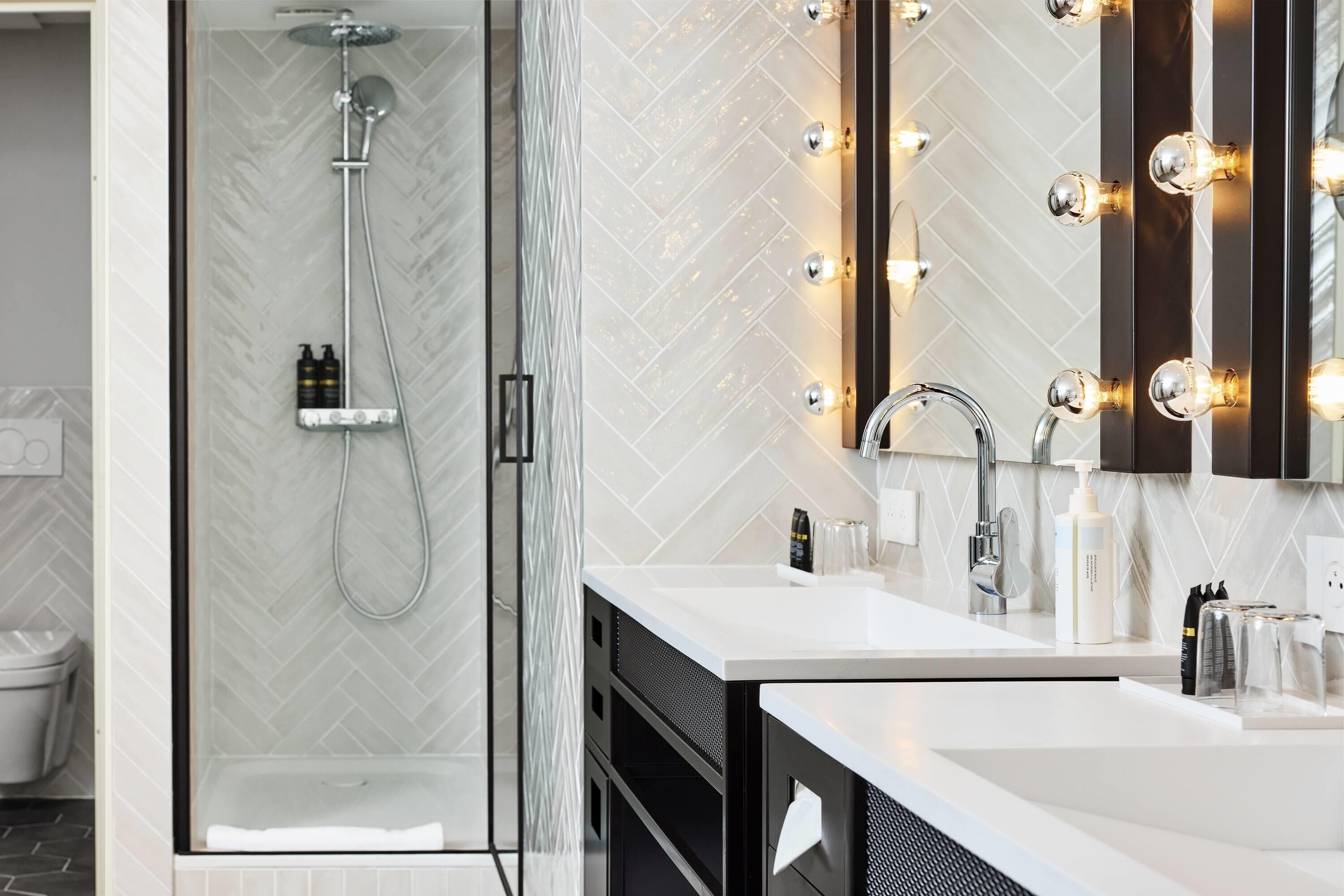 A modern bathroom with a glass-enclosed shower, a vanity with a mirror, and wall-mounted lights.