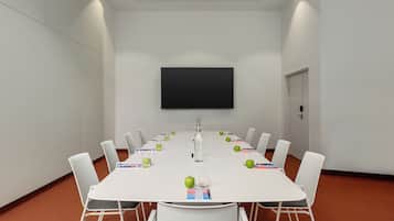 A conference room with a white table, chairs, a flat-screen TV, and green apples on the table.