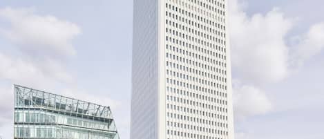 A modern high-rise building with a grid-like facade, surrounded by a landscaped area with a curved glass structure.