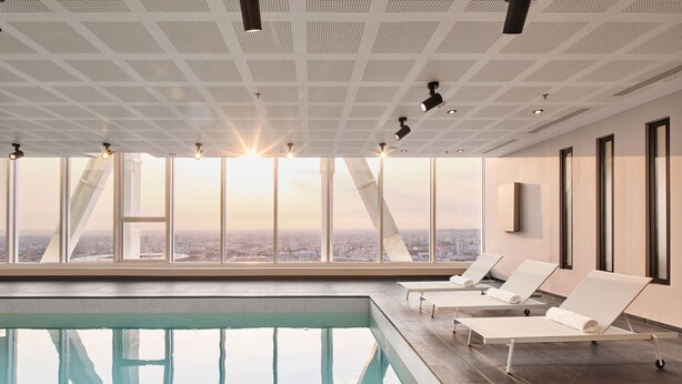 An indoor swimming pool with lounge chairs and large windows offering a city view. - H4 Wyndham Paris Pleyel (Saint-Denis)