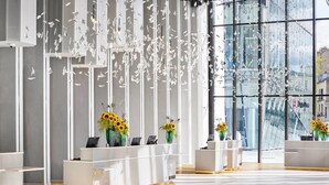 A modern reception area with a glass wall, white reception desks, and sunflowers. - H4 Wyndham Paris Pleyel (Saint-Denis)