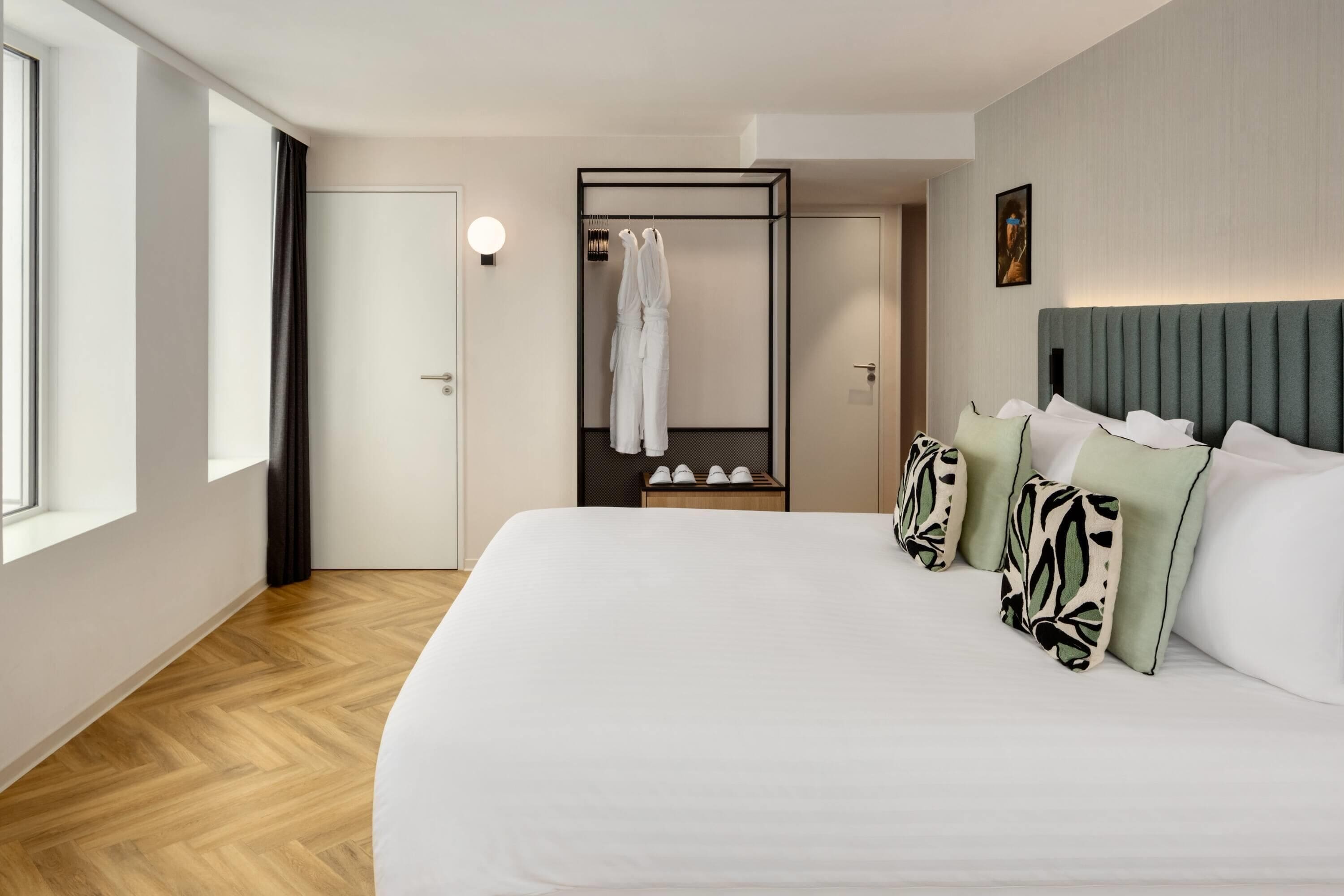 A hotel room with a large bed, a wardrobe, a mirror, and a shoe rack.
