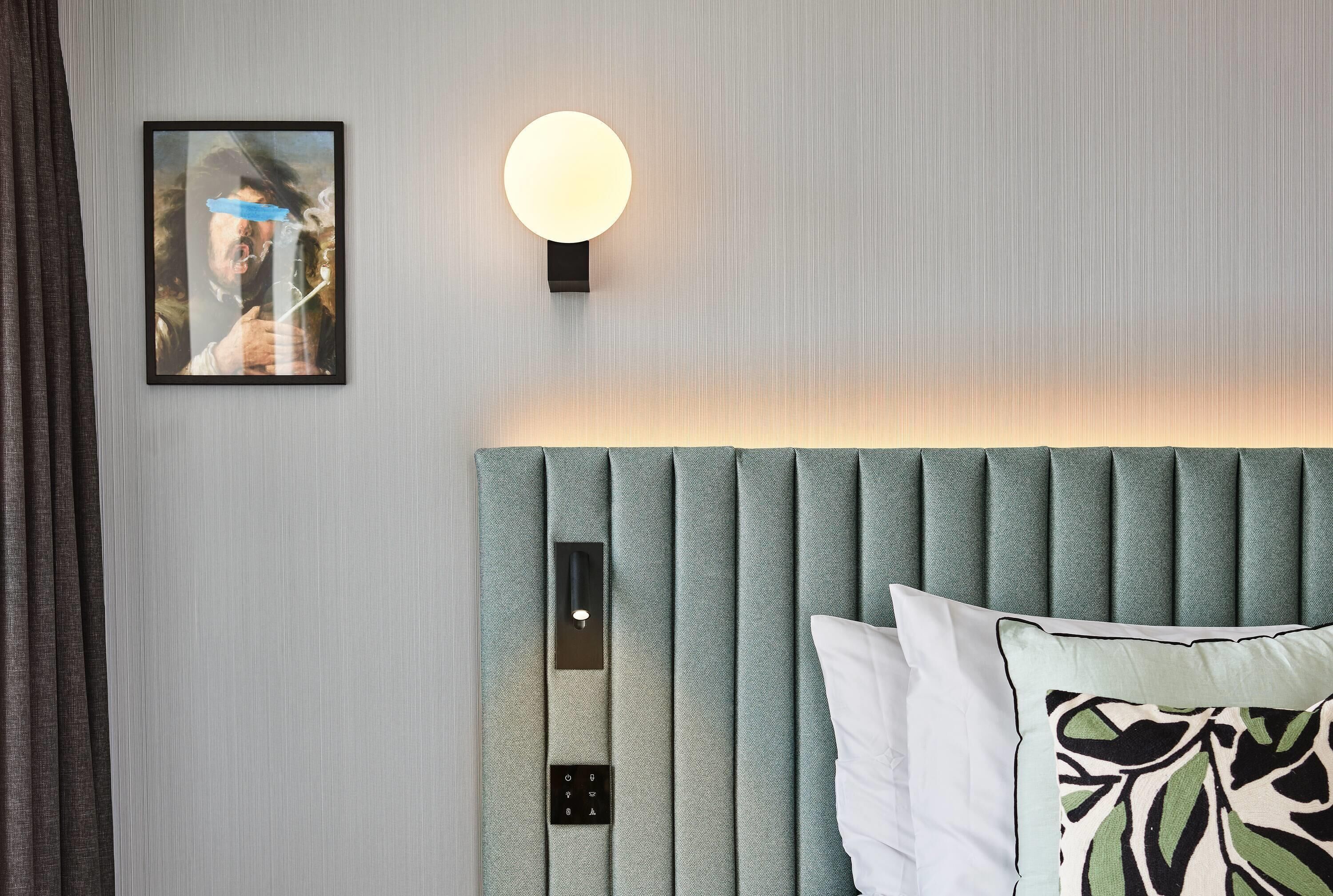 A modern room with a headboard, a wall-mounted light, a framed picture, and a control panel.