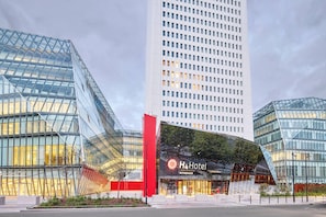 A modern hotel with a glass facade, a prominent red vertical element, and a sign reading 'H4 Hotel'. - Wyndham Paris Pleyel (Saint-Denis)