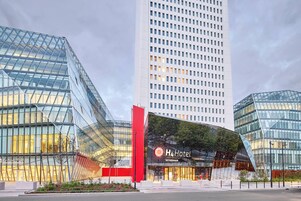 Un hotel moderno con facciata in vetro, un elemento verticale rosso ben visibile e un cartello con la scritta 'H4 Hotel'.