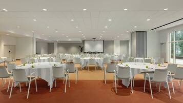 A conference room with multiple tables and chairs, a large screen at the front, and a carpeted floor.
