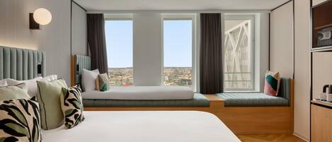 Una habitación de hotel moderna con una cama grande, una zona de estar con vistas y una pequeña kitchenette.