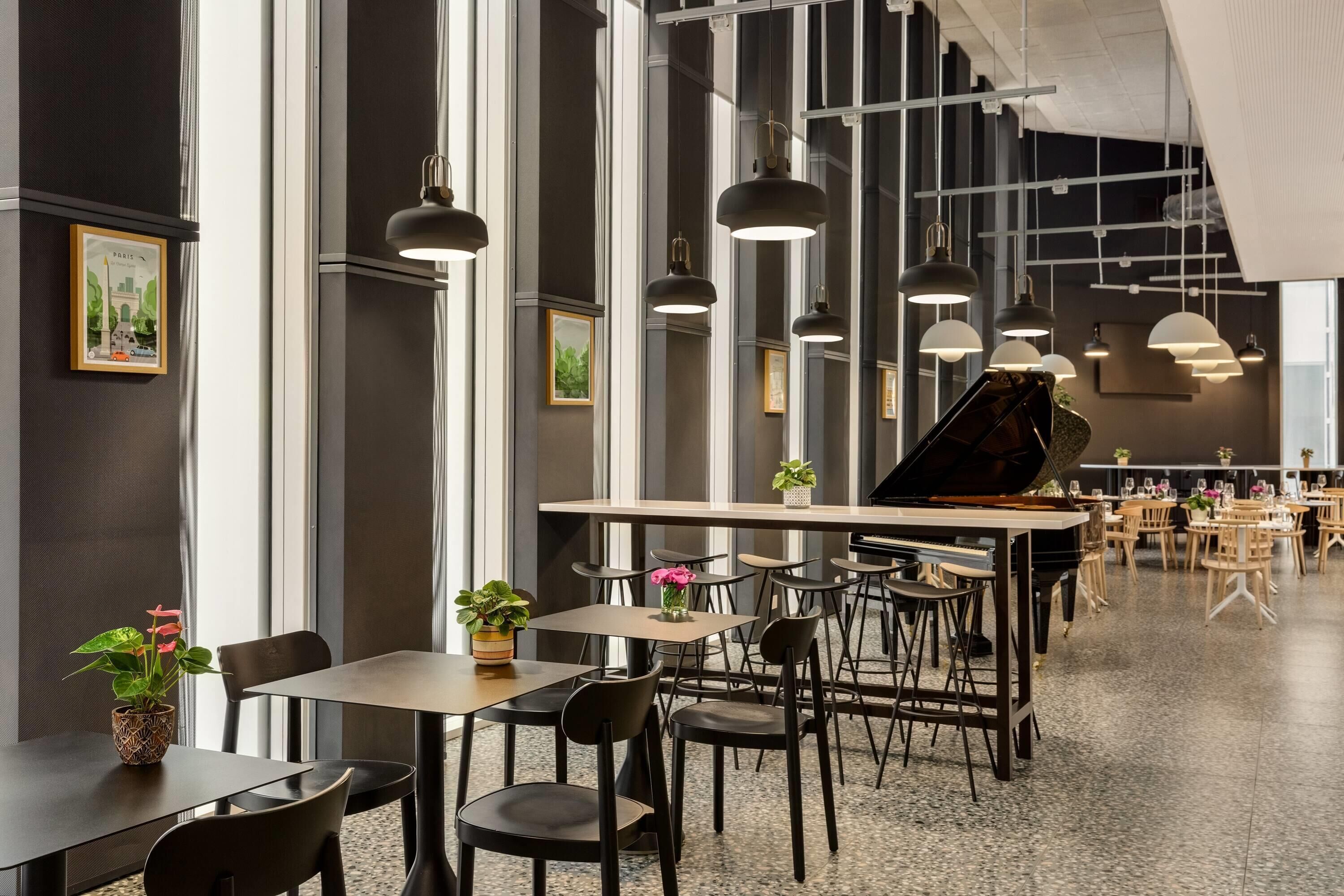 A spacious indoor area with multiple tables and chairs, a grand piano, and pendant lighting.