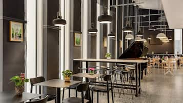 A spacious indoor area with multiple tables and chairs, a grand piano, and pendant lighting.