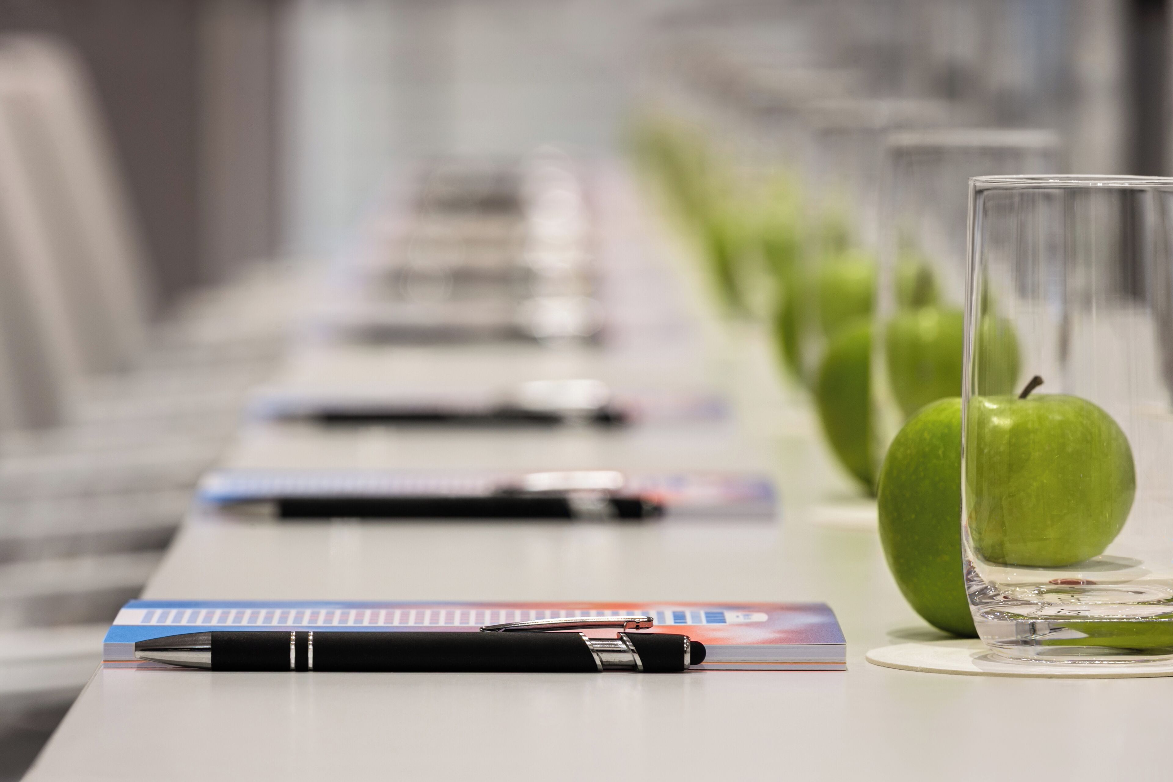 A table with pens, a glass, and an apple.