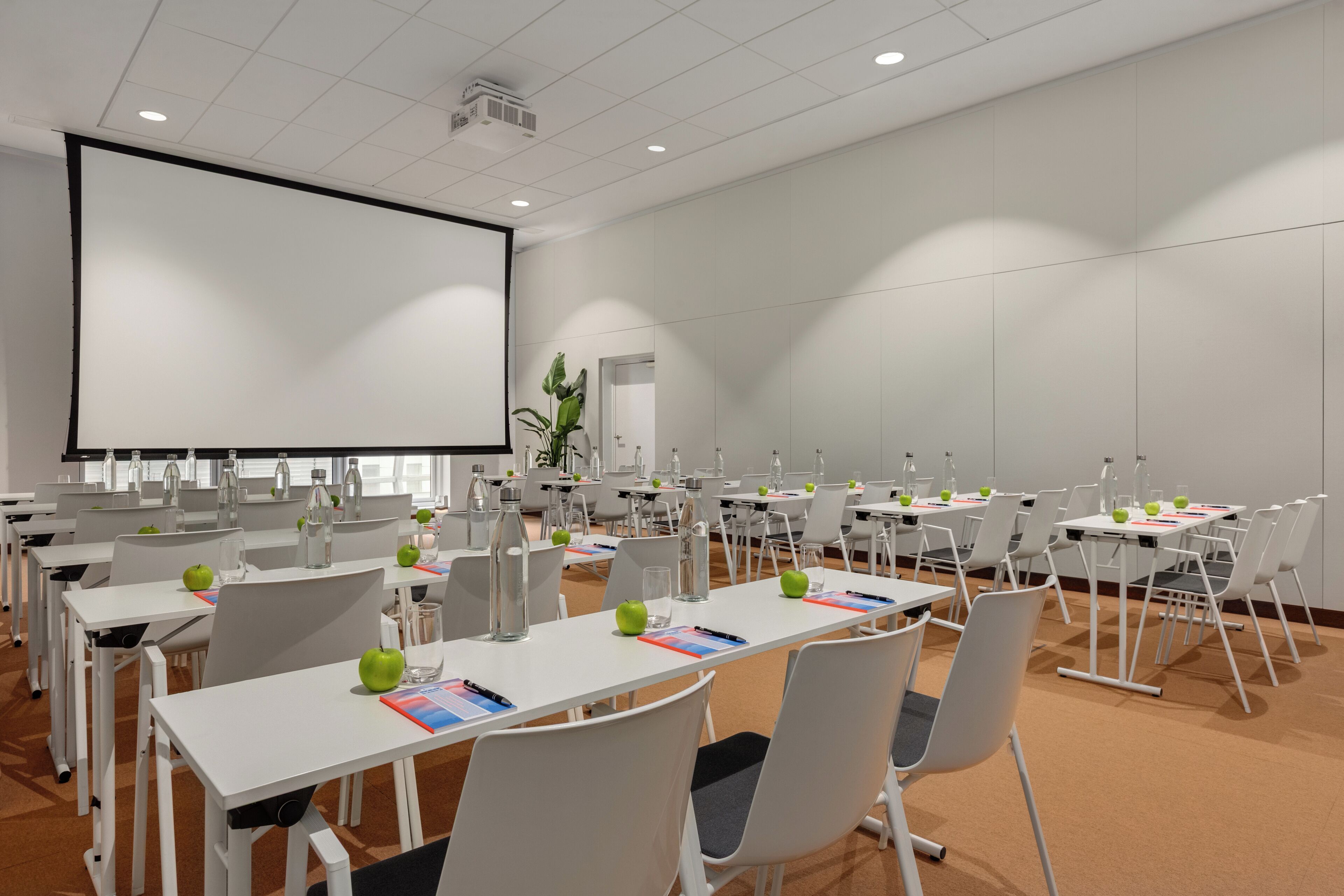 A conference room with white tables, chairs, and a large screen.