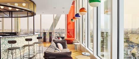 A modern interior with a bar area, seating, and large windows offering city views.