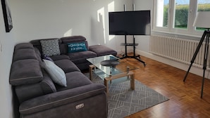 Un salon comprenant un canapé, une table basse en verre, un téléviseur à écran plat et un trépied.