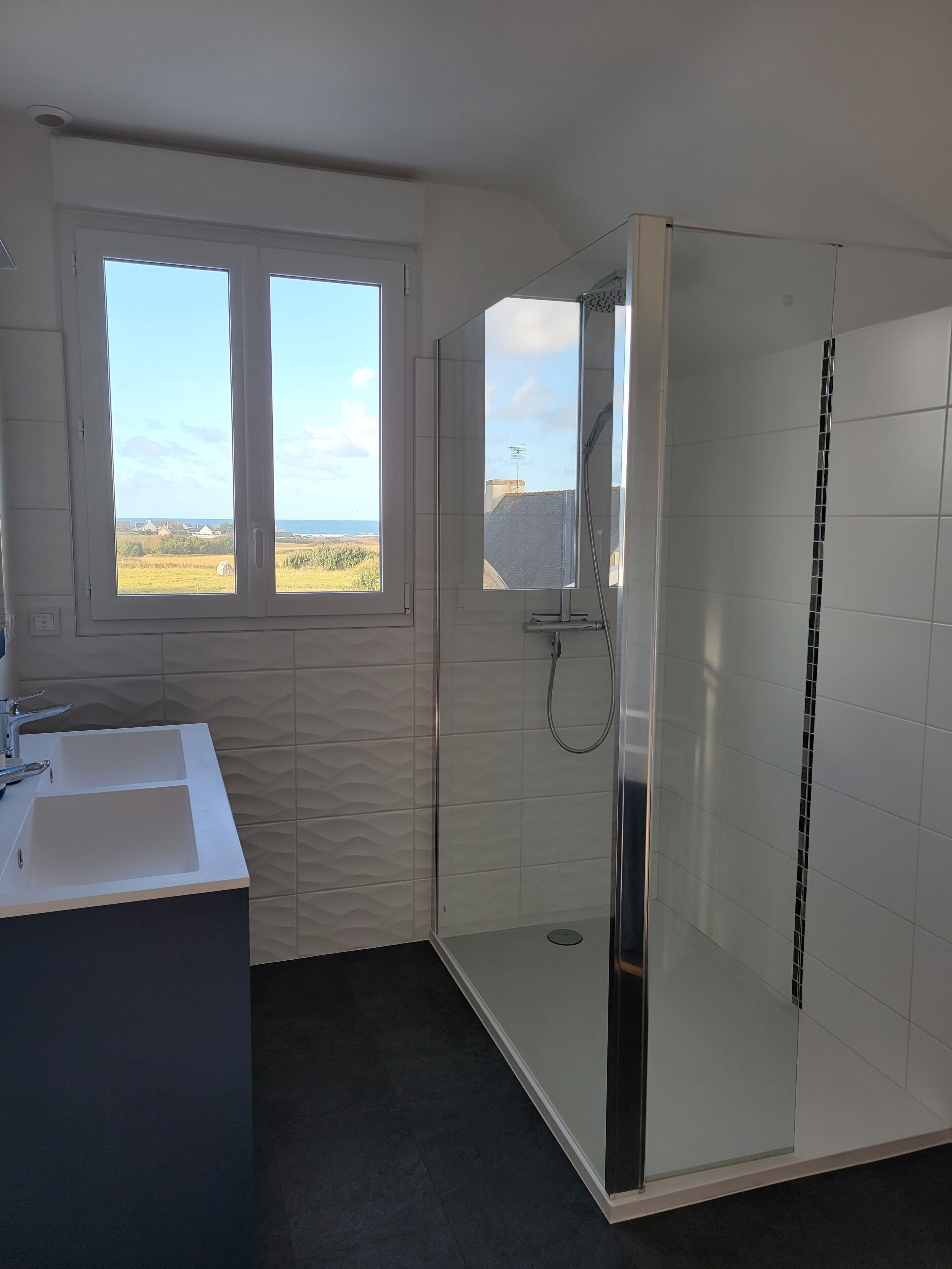 Une salle de bain moderne équipée d’une douche, d’un lavabo et d’une fenêtre donnant sur la campagne.