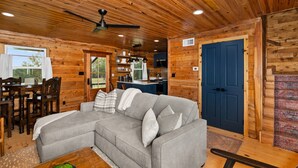 A cozy cabin interior with a gray sectional sofa, wooden walls, a dining area, and a kitchen. - The Hendo - Cabin #2- Intimate Family Getaway (Henderson)