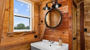 A wooden cabin bathroom with a white sink, two wall-mounted lights, and a round mirror. - The Hendo - Cabin #2- Intimate Family Getaway (Henderson)