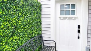 A white door with a window, a black metal bench, and a green hedge. - Private & cozy suite located in Fort Langley (Langley Township)
