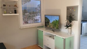 A modern living room with a flat-screen TV, a decorative vase, and a window with curtains. - München Waldperlach Ruhig und Großzügige Wohnung (München)
