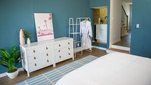 Un dormitorio con cama, cómoda y un tendedero de metal blanco con ropa.
